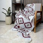 شال مبل طرح‌دار هندسی سایز دو نفره رنگ زرشکی پهن شده روی کاناپه راحتی