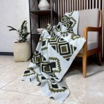 شال مبل طرح‌دار هندسی سایز دو نفره رنگ سبز زیتونی پهن شده روی کاناپه راحتی